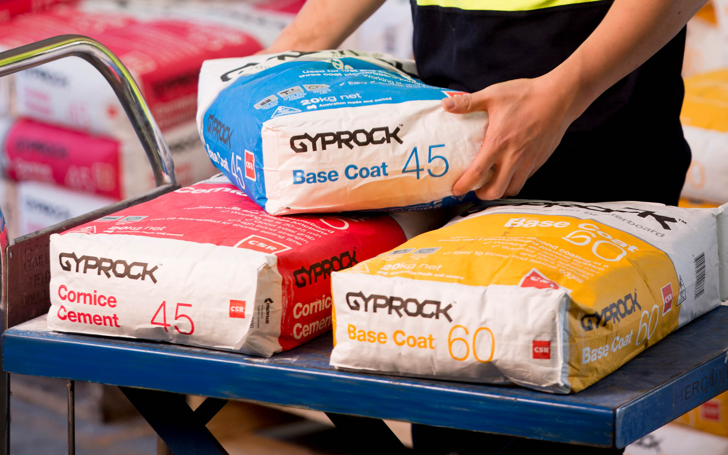 Gyprock worker holding a Base Coat bag over two other Gyprock products