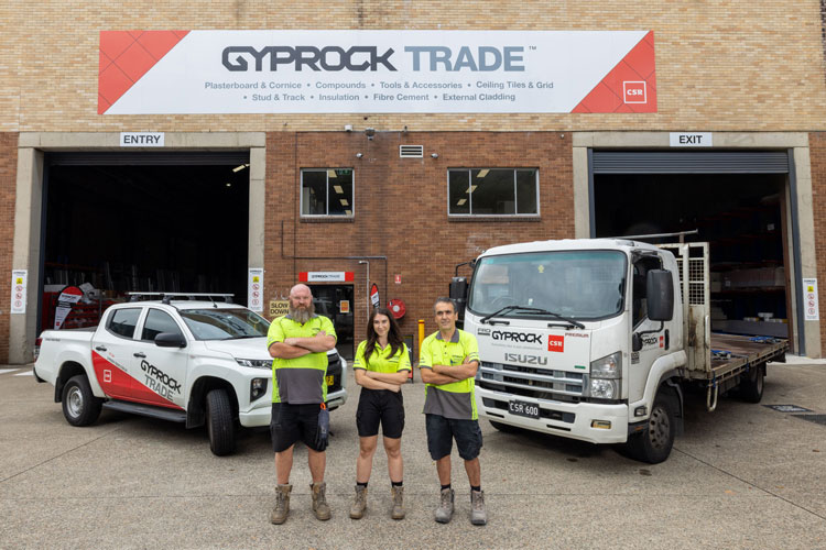 Gyprock Trade Centre with three Gyprock specialists in hi-visibility shirt in front of Gyprock Trade vehicles.