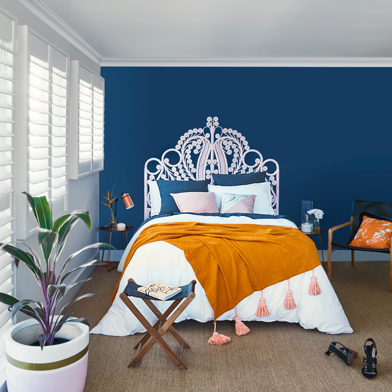 Bedroom with blue wall, a bed with an ornamental headboard, indoor plant and fold-out side table.