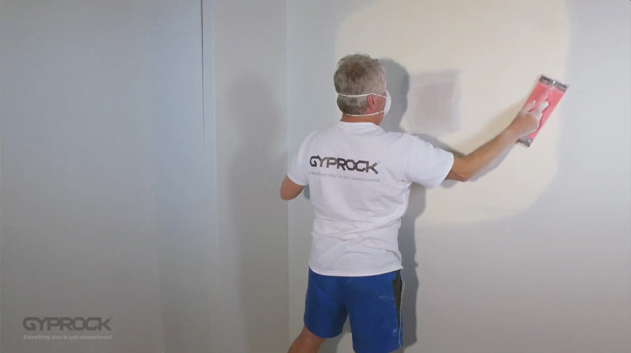 Gyprock installer wearing PPE sanding down plaster on the wall