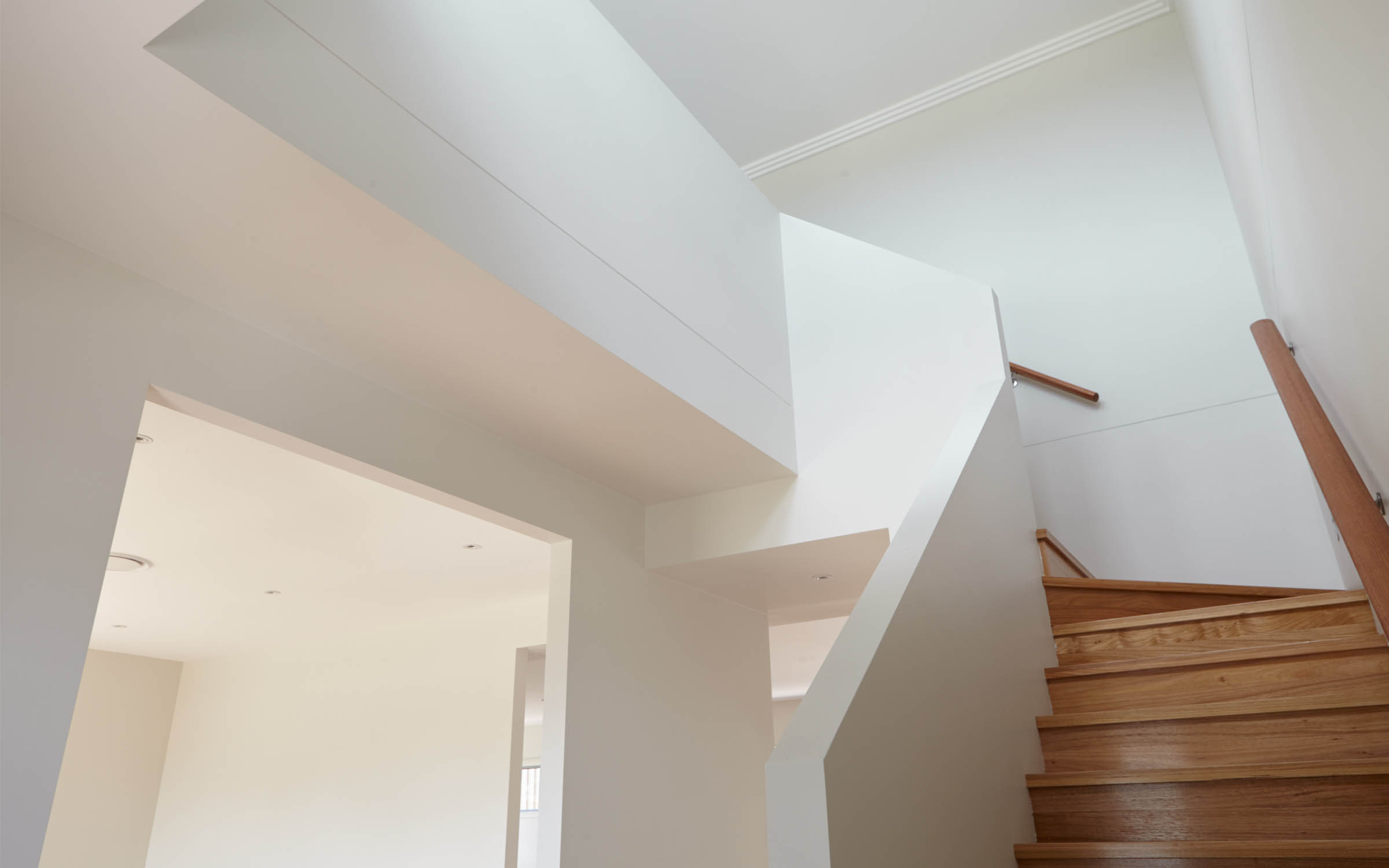 Staircase to second storey with wooden stairs and white walls.