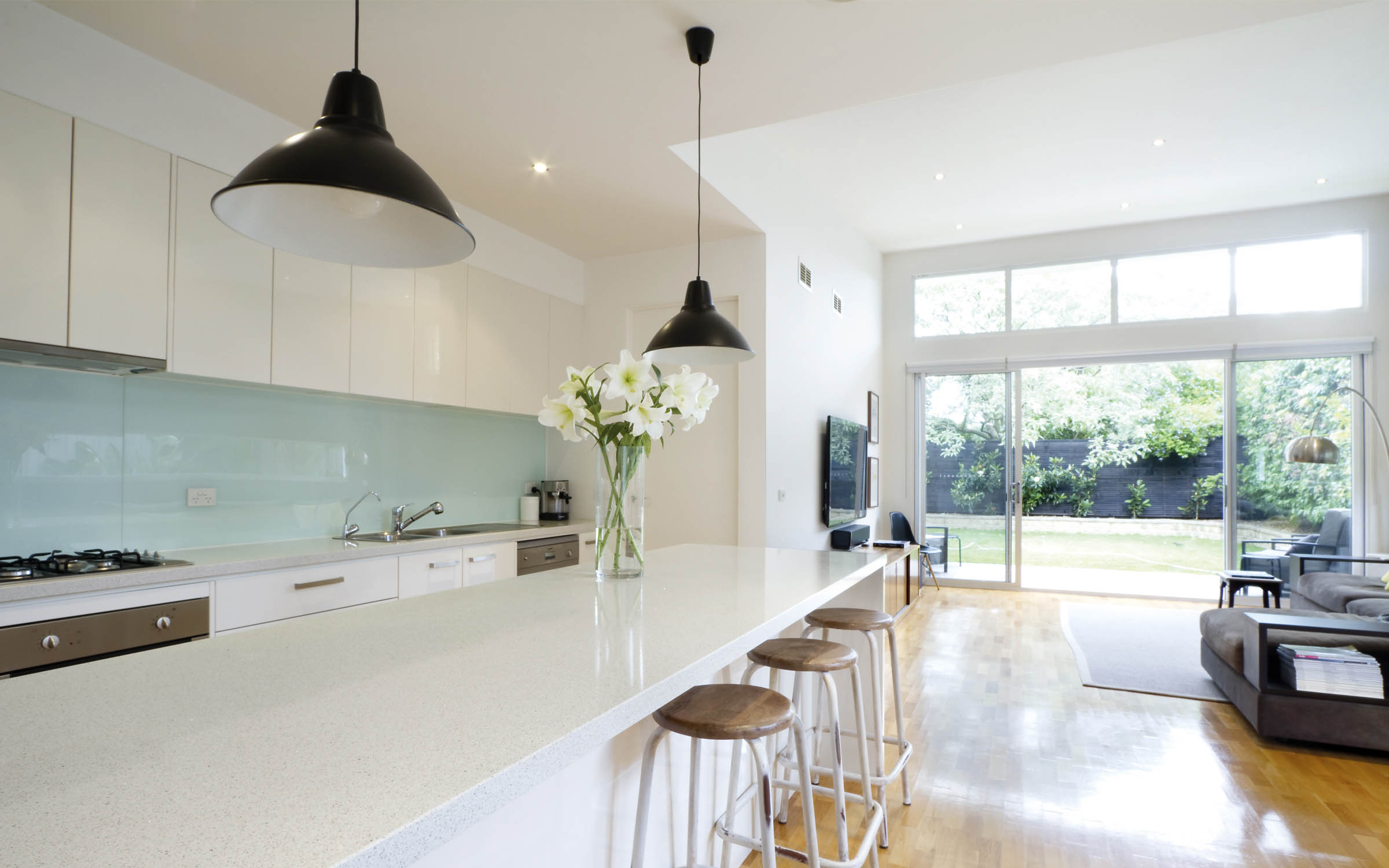 Kitchen area with stone island bench, stools, and a view of the backyard.