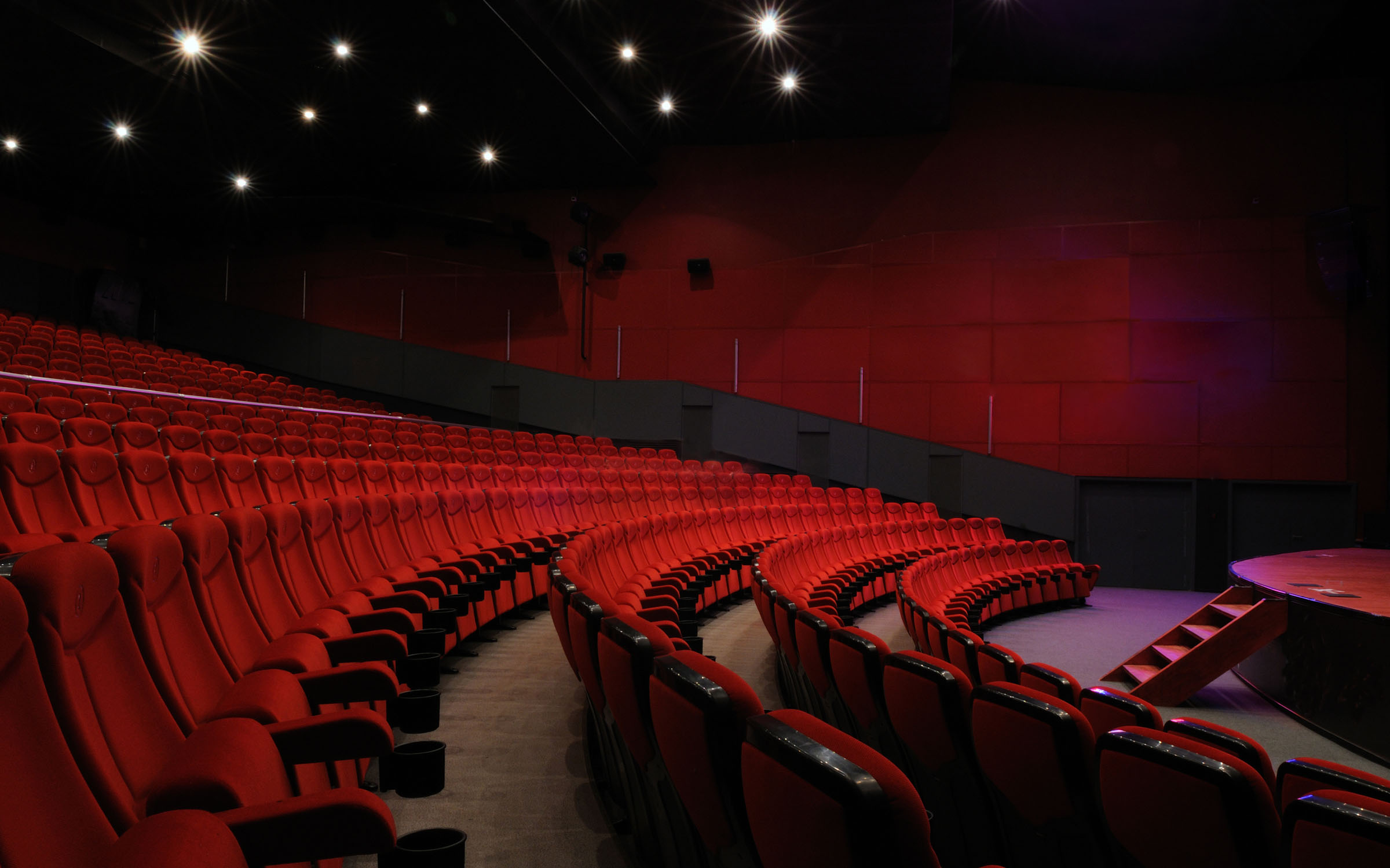 Large cinema with red chairs in a curved circular layout.