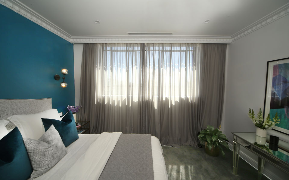 Bedroom with a blue feature wall and sunlight coming through sheer curtains.