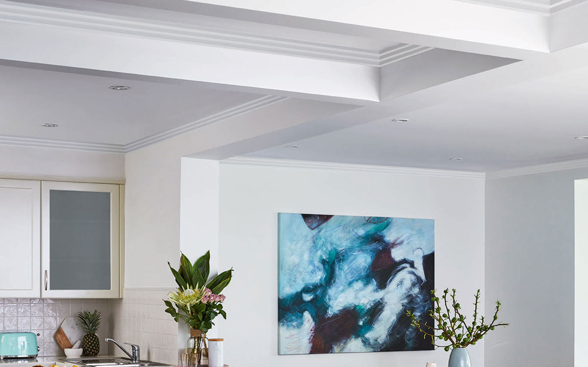 Bold ceiling details with cornices in a designer styled room with artwork and floral arrangements.