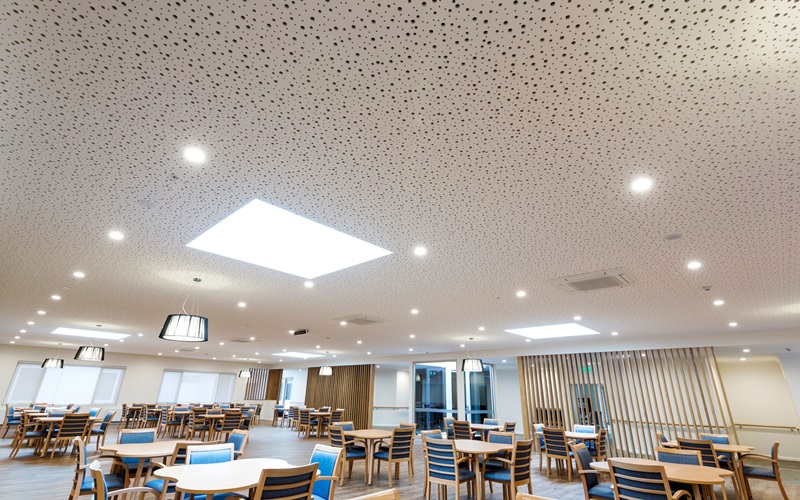 Large breakout space with tables, chairs, and emphasis on the ceiling panel and lighting.