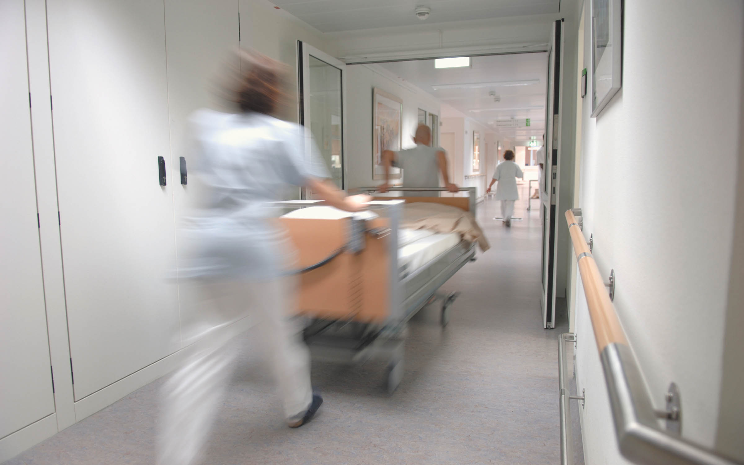 Commercial healthcare facility hallway with healthcare professionals moving a hospital bed.